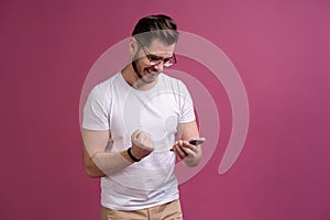 Always in touch. Smiling young man holding smart phone and looking at it. Portrait of a happy man using mobile phone