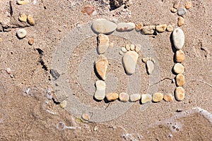 Touching picture of sea pebbles on  sandy beach. Image of a child`s and adult`s foot made of stones. Ebbles and sand in the sea.