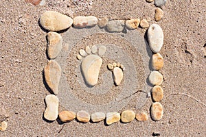 Touching picture of sea pebbles on  sandy beach. Image of a child`s and adult`s foot made of stones. Ebbles and sand in the sea.