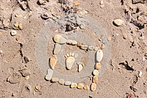 Touching picture of sea pebbles on  sandy beach. Image of a child`s and adult`s foot made of stones. Ebbles and sand in the sea.