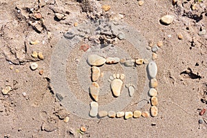 Touching picture of sea pebbles on  sandy beach. Image of a child`s and adult`s foot made of stones. Ebbles and sand in the sea.