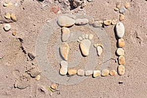 Touching picture of sea pebbles on  sandy beach. Image of a child`s and adult`s foot made of stones. Ebbles and sand in the sea.