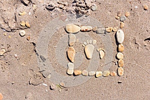 Touching picture of sea pebbles on  sandy beach. Image of a child`s and adult`s foot made of stones. Ebbles and sand in the sea.