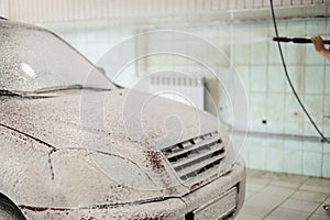 At a touchless car wash the driver applies foam from a gun. The red car is covered with soap suds in the box of the