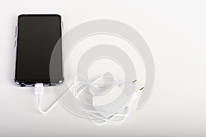 Touchscreen smartphone and white charger and white cable for charging  in white background