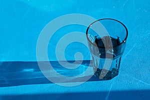 Tough, abstract shadow from a transparent glass with drinking water on a blue background. Selective focus, copy space