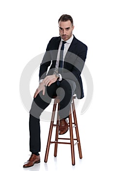 Tough businessman leaning on his leg, sitting on a stool