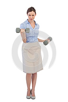 Tough businesswoman lifting dumbbells looking at camera