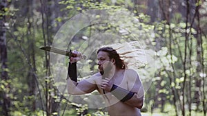 Tough guy looking like a medieval warrior training with a knife in the woods.