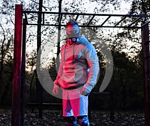 Tough strong muscular man wearing a workout mask standing below horizontal ladder in the park taking a break during workout