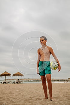 Tough wet boy holding volleyball ball on the beach