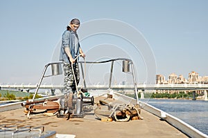 Tough young man standing on boat and tying rope sailing in city waters