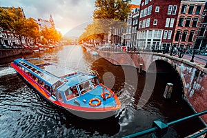 Tour boat at famous Dutch canal on sunset evening. Traditional Dutch bridges and medieval houses. Amsterdam Holland photo