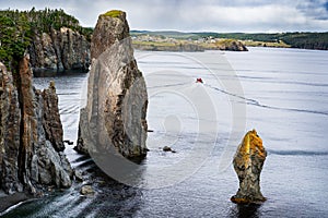 A tour boat travelling near high rocky cliffs along the Skerwink hiking trail on the East Coast of Canada