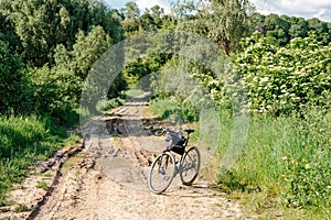 A touring bicycle stands in the middle of a dirt road with puddles and mud in the countryside. A bicycle stands on a forest path.
