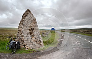 Touring bike leans against a large stone cairn, or currick, at Shorngate Cross on the border of Northumberland and County Durham,