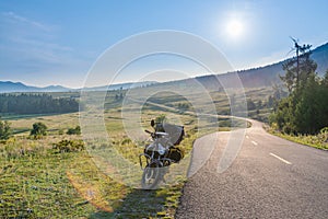 Touring motorcycle parking on asphalt road passing through grassland with sunbeams