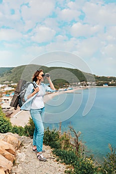 Tourism and active recreation. A young woman with a backpack looks through binoculars. In the background, the mountain