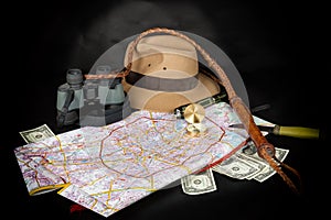 Tourism and adventure concept. Compass on city map with flashlight, fedora hat, bullwhip, binocular, knife and dollar bills on dar