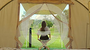 Tourism concept. Back view of travel woman relax outside the modern camp tent. Dawn in a forest with a lonely tent