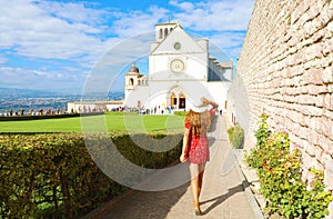 Tourism in Italy. Back view of beautiful girl with red dress walking towards the Basilica of Saint Francis of Assisi in Umbria,