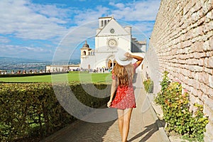 Tourism in Italy. Back view of beautiful girl walking towards the Basilica of Saint Francis of Assisi in Umbria, Italy