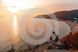 Tourism and sports recreation. A young woman with a tourist backpack on her back sits on a rock and looks at the sunset and the