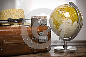 Tourism and travel concept. Globe and vintage suitcase with summer hat, sunglasses photo camera on wooden table