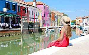 Tourism in Venice. Panoramic banner view of pretty woman in red dress sitting and looking the old colorful town of Burano in