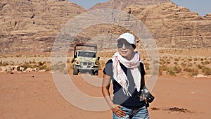 Tourist Asian woman carrying camera in Wadi Rum desert, Jordan with safari car behind.