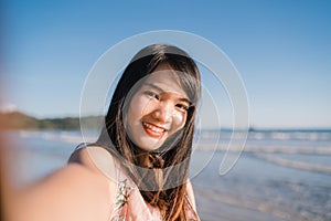 Tourist Asian woman selfie on beach, young beautiful female happy smiling using mobile phone taking selfie on beach near sea when