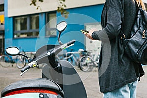 A tourist with a backpack is going to use an electric scooter through a mobile application in the phone and distally