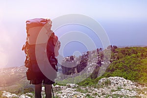 Tourist with a backpack looking from the mountains to the sea. Hiking in the mountains of Crimea. View of the forest and the city