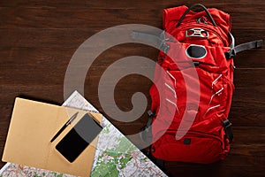 Tourist backpack with map, notebook, pen and telephone on the wooden background.