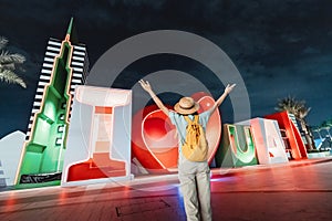 Tourist with a backpack poses and enjoys her journey near the caption I love Dubai at night. Sightseeing attractions in UAE
