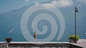 Tourist with backpack stands on stone pier and enjoy lake view, Alps mountains