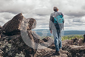 A tourist with a backpack stands on the top of the mountain and admires the view. The concept of sports and active life