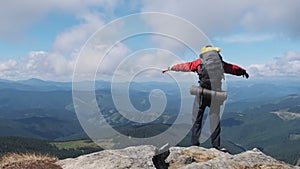 Tourist with Backpack on the Top of Mountain near the Cliff Raises Hands to Side
