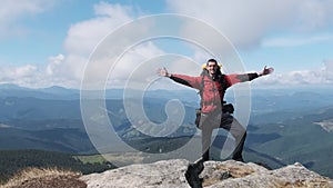 Tourist with Backpack on the Top of Mountain near the Cliff Raises Hands to Side