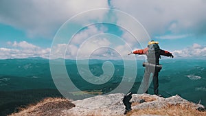 Tourist with Backpack on the Top of Mountain near the Cliff Raises Hands to Side