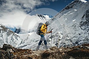 Tourist with backpack and trekking poles walks along mountain track. Solo hiker traveling among altitude cloudy mountains