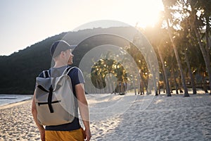 Tourist with backpack walking on beautiful beach with palm trees at sunset