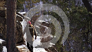 A tourist with a backpack walks along a cliff in the middle of a winter snow forest. Active recreation and hiking