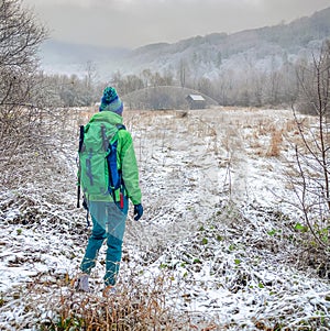 Tourist backpacker traveler with a green backpack goes on a trekking route in the winter in the forest in frosty weather