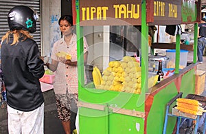 Tourist bargaining with steamed corn seller in the street, in Bali.