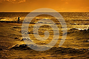 Tourist on Beach with Ocean and Golden Sunrise Sunset Light