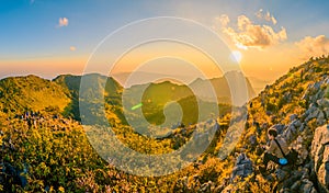 A tourist with beautiful mountain peaks topped with vivid sky, cloud and blast horizon sun, and decorated with camera flares