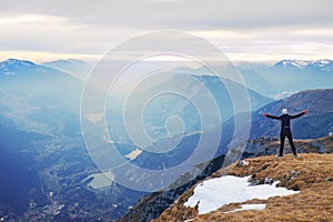 Tourist in black is standing on rocky view point and watching into misty rocky mountains. Fogy winter morning in Alps..