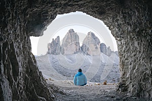 Tourist in blue jacket at cave in mountain against Three peaks of Lavaredo