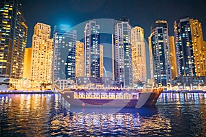 Tourist Boat, Sightseeing Boat Sailing On Dubai Marina At Nighttime. Night View Of high-rise buildings of residential